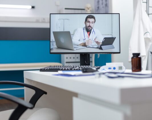 Computer screen with remote doctor having online videocall meeting Computer screen with remote doctor having online videocall meeting conference standing on table in empty hospital office. Telework videoconference call during medical consultation. Medicine concept