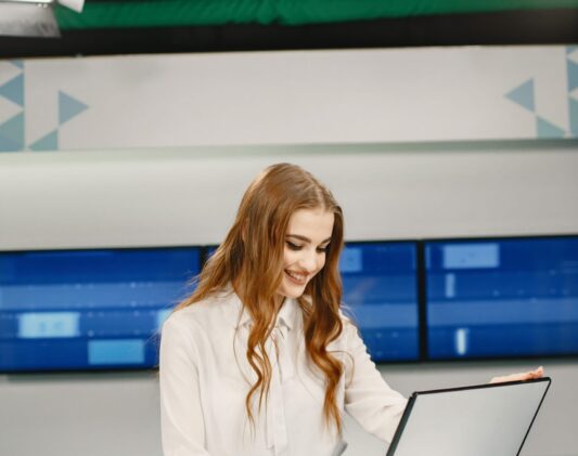 Young pretty tv presenter in studio before broadcasting Tv present at studio preparing for new broadcasting. Smiling girl in white shirt sitting at table .