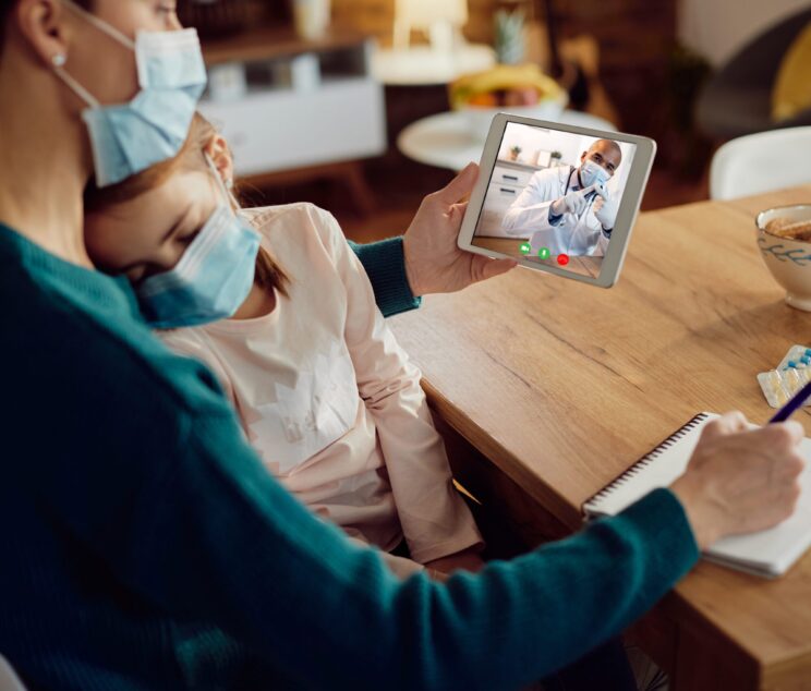 Close-up of mother using digital tablet while talking with pediatrician about her ill daughter during coronavirus pandemic.