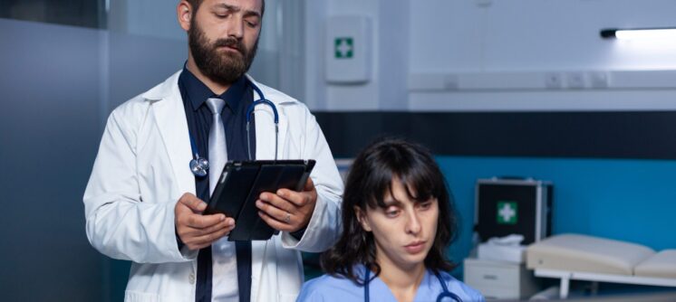 Team of medical workers using technology for overtime work. Doctor holding digital tablet for information while woman nurse looking at computer on desk for healthcare, working late.